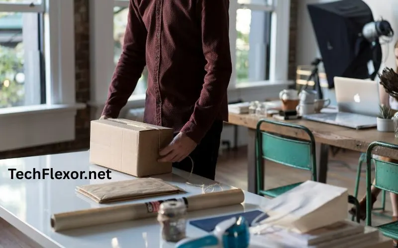 Person packing a small box on a desk in a modern office workspace with laptop and supplies. This Image shows benefits of byod.